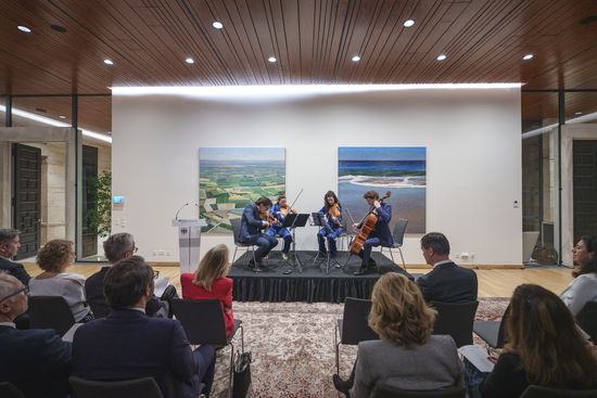 Veranstaltung in der deutschen Botschaft mit einem Streichquartett, das auf einer Bühne vor einem Publikum in einem modernen Saal mit Kunstwerken an der Wand spielt.