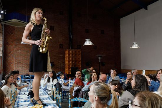Eine der Musikerinnen auf einem Tisch stehend, während sie Saxofon spielt, umgeben von begeisterten Zuschauern