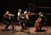 Los 4 artistas sentados tocando sus instrumentos en escenario