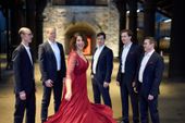 Foto alegre de los miembros de Singer Pur en traje formal alrededor de la soprano en un vestido rojo
