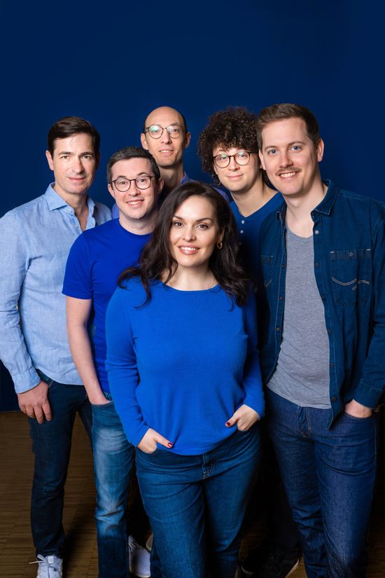 Die sechs Mitglieder der Gruppe lächeln in die Kamera. Alle sind blau angezogen, ganz vorne steht eine Frau. Die anderen sind Männer.